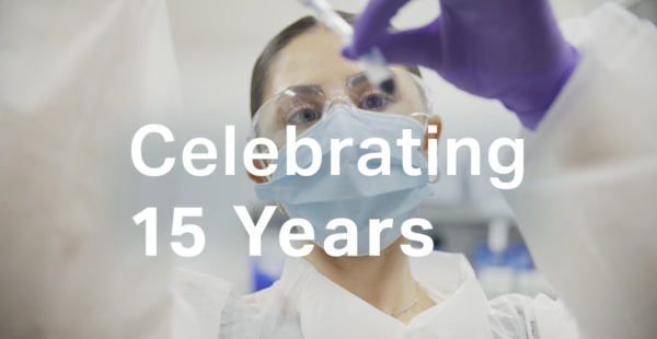 A scientist wearing safety glasses and a mask conducts an experiment. Text overlay reads, "Celebrating 15 Years.